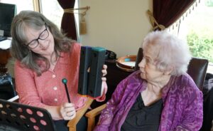 Photo of Music Therapist Winifred Beevers in a music therapy session with Cynthia Turner. Winifred is holding and playing a percussion instrument.