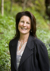 A photo of Bridgit Hogan, CEO of Australian Music Therapy Association, smiling, with greenery in the background